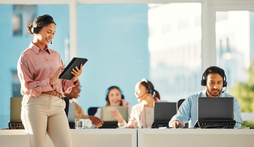 A call center trainer standing with a tablet next to employees working