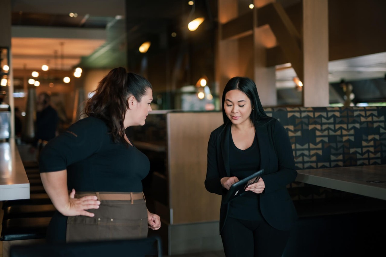 A manager showing something on an electronic tablet to a colleague waitress