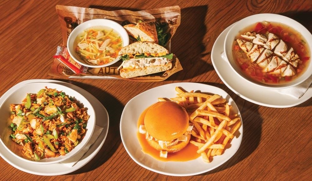 4 lunch meals on a table in a St-Hubert restaurant: the chicken sandwich with soup, chicken rice, Hearty chicken and vegetable soup, and the BBQ sandwich.