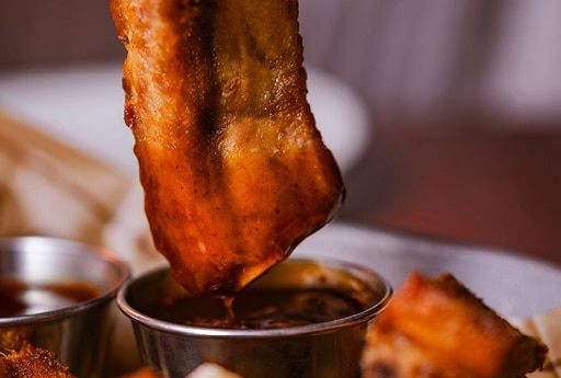 Someone who dips their ribs in a sauce, on a plate, at the table